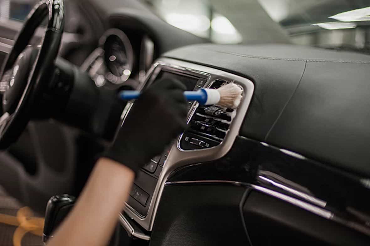 На фото мастер детейлинг-центра AR-Detailing с помощью кисти и моющего средства удаляет грязь из решетки воздуховода автомобиля.